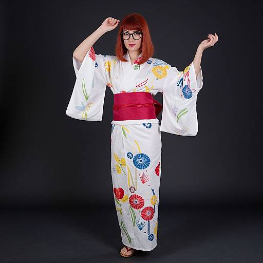 Photograph of a red-haired woman with glasses, wearing a white floral kimono, red obi, and sandals, posing against a black background.