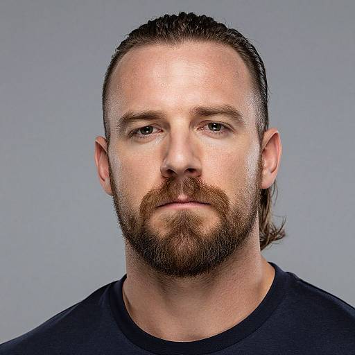 Photograph of a Caucasian man with long brown hair, beard, and mustache, wearing a black shirt, against a plain gray background.