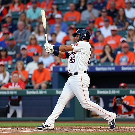 Photograph of a baseball player in white uniform, mid-swing, with black helmet and blue gloves, against a blurred crowd in orange.