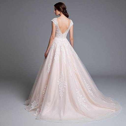 Photograph of a woman with dark hair in an elegant white lace wedding gown, viewed from the back, standing against a plain gray background.