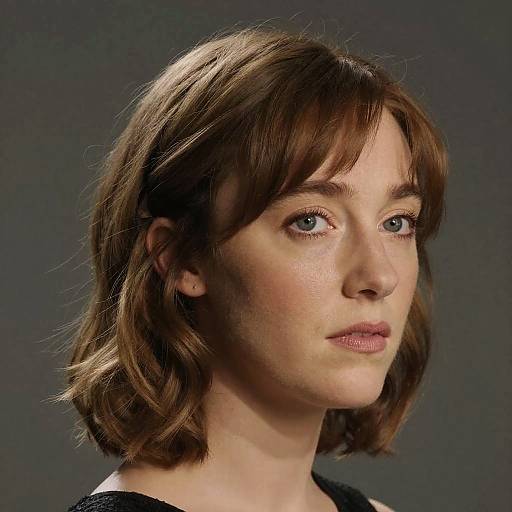 Photograph of a Caucasian woman with short brown hair, blue eyes, and fair skin, wearing a black top, against a dark gray background.