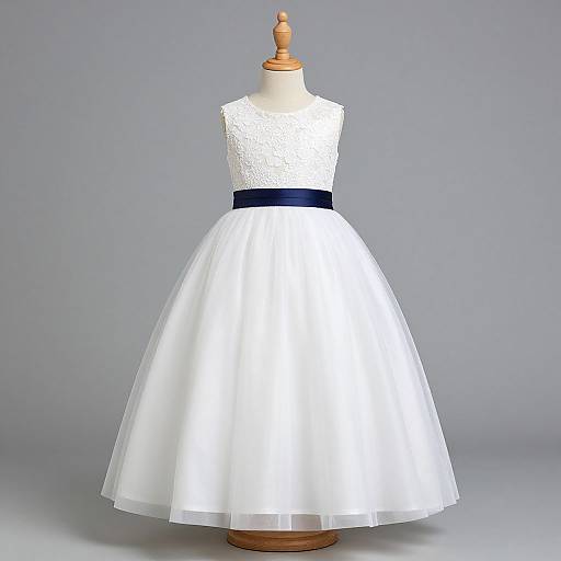 Photograph of a white lace sleeveless dress with a navy blue waistband, full tulle skirt, displayed on a wooden dress form against a gray