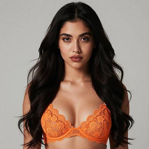 Photograph of a young woman with long black hair, wearing an orange lace bra, against a plain light gray background.