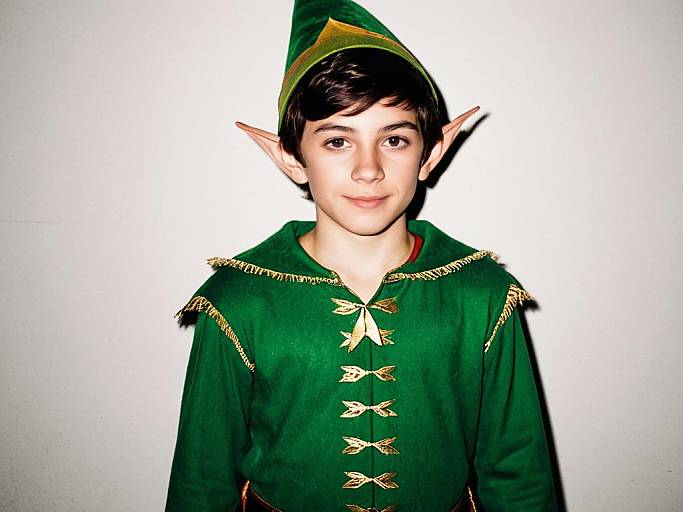 Photograph of a young boy with fair skin and dark hair, wearing a green elf costume with gold accents, pointed ears, and a matching hat,