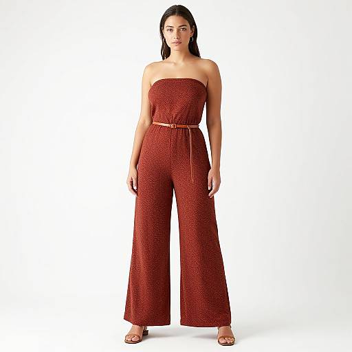 Photograph of a woman with long dark hair, wearing a strapless, red, high-waisted jumpsuit with a belt, standing against a