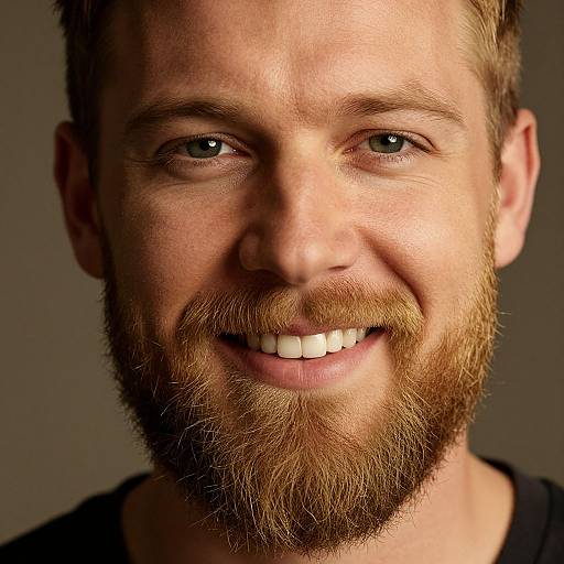Close-up photograph of a smiling Caucasian man with light brown beard, blue-green eyes, and short brown hair against a dark background.