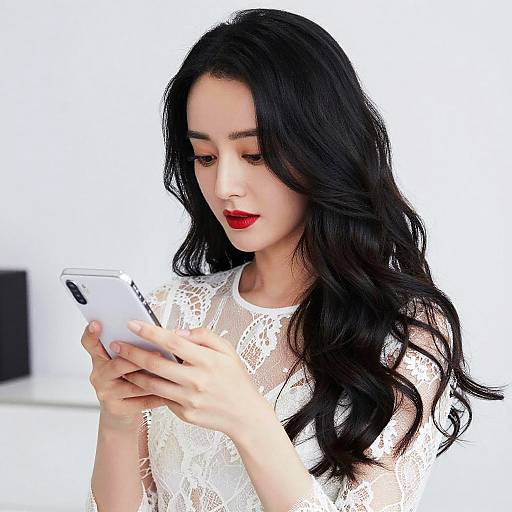 Photograph of a young woman with long black wavy hair, fair skin, red lipstick, wearing a white lace top, intently looking at a
