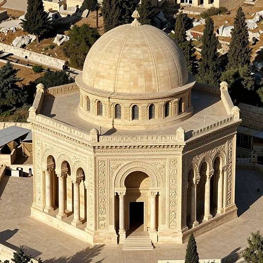 Aerial photograph of an ornate, sunlit, beige-domed building with intricate arches and carvings, surrounded by trees and rooftops