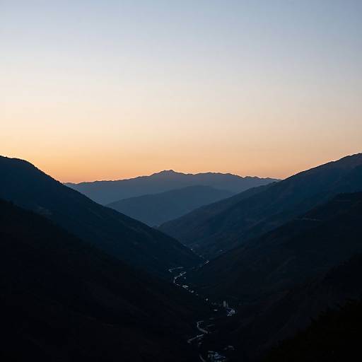 Photograph of a serene mountain landscape at sunrise, with dark silhouetted hills in the foreground and a gradient sky transitioning from orange to blue in
