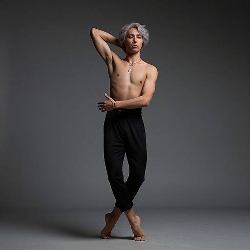 Photograph of a shirtless, muscular Asian man with gray hair, wearing black pants, standing barefoot against a gradient gray background, posing with one