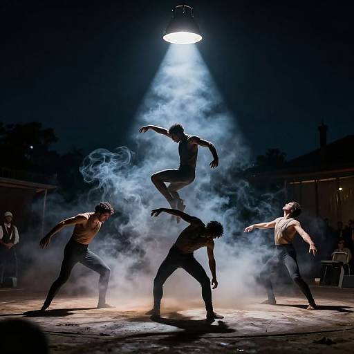 Photograph of five male dancers in silhouette, performing acrobatics on stage, illuminated by a bright spotlight amidst swirling fog.