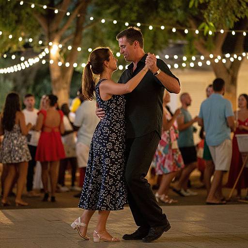 Photograph of a dancing couple in a dimly-lit outdoor setting with string lights, wearing a black shirt and blue floral dress. Background shows other