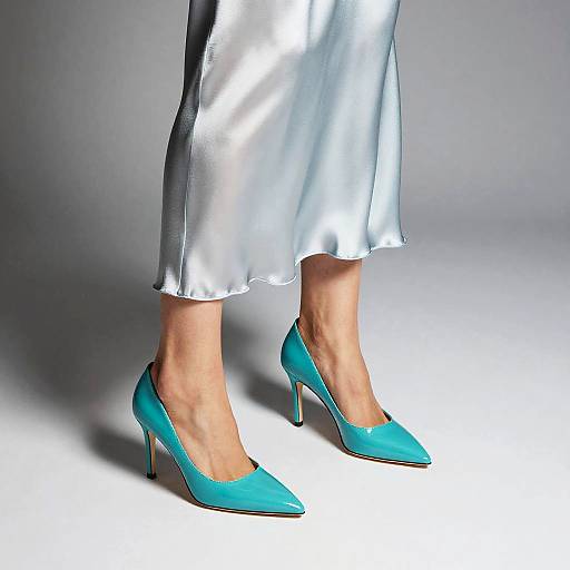 Photograph of a person's legs wearing shiny silver satin pants and vibrant turquoise pointed high heels against a gray background.