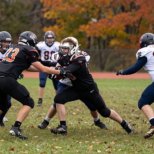 Photograph of intense football game: Black-clad player with white helmet runs, dodging tacklers in black and white uniforms, autumn field background.