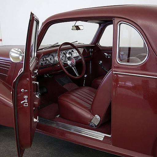 Photograph of a vintage, maroon classic car's interior with open driver's door, showcasing leather seats, chrome dashboard, and vintage steering wheel.