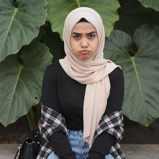 Photograph of a young South Asian woman with a light brown complexion, wearing a white hijab, black long-sleeve top, blue jeans,