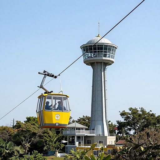 Photograph of a yellow cable car with passengers, ascending beside a tall, gray observation tower with a circular top, set against a clear blue sky and