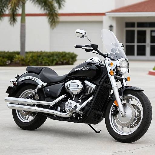 Photograph of a black Harley-Davidson motorcycle with chrome accents, clear windshield, and orange turn signals, parked in front of a modern building with