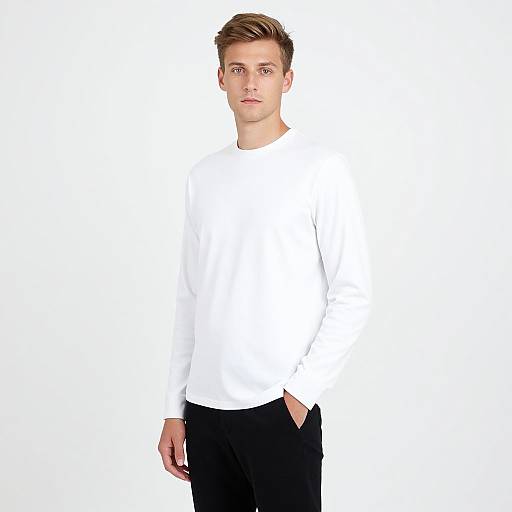 Photograph of a young Caucasian man with short, styled brown hair, wearing a white long-sleeve shirt and black pants, standing against a plain