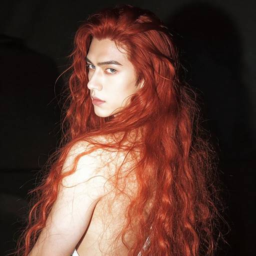 Photograph of a pale-skinned woman with long, wavy red hair, looking over her shoulder against a black background. Her intense gaze is highlighted