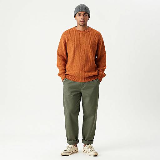 Photograph of a young man with medium skin tone, wearing an orange knitted sweater, dark green pants, white sneakers, and a gray knit be