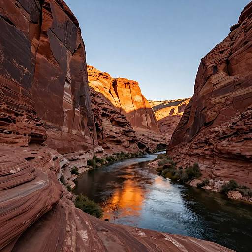 Photograph of a stunning desert canyon at sunset, featuring towering red rock cliffs, a reflective river, and vibrant orange sunlight.