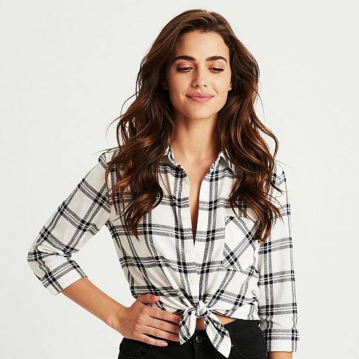Photograph of a smiling woman with long brown hair, wearing a white plaid shirt tied at the waist, black pants, and white background.
