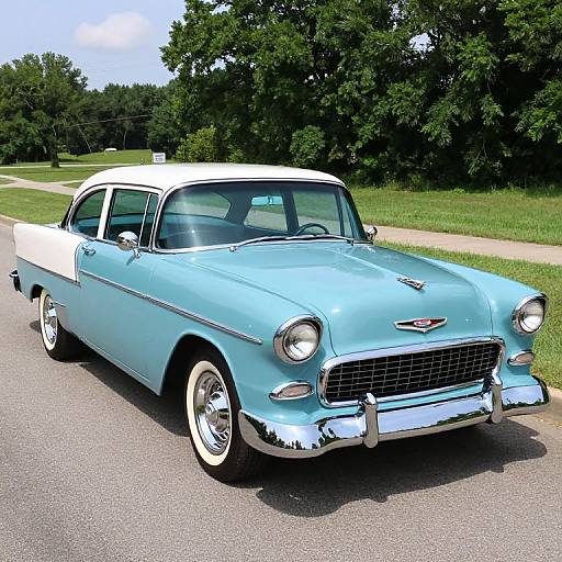Photograph of a classic light blue and white vintage sedan with chrome accents, white-walled tires, parked on a sunny rural road.