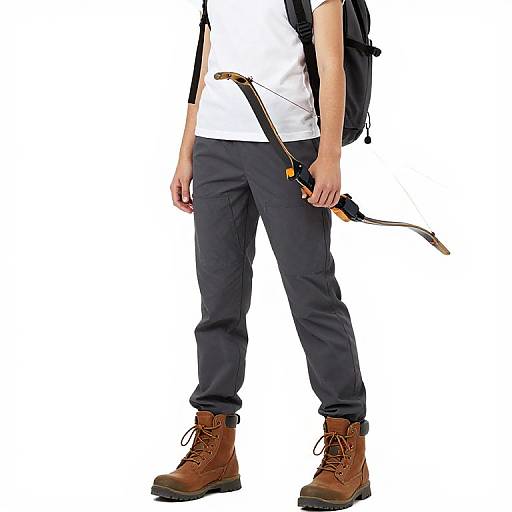 Photograph of a person wearing a white shirt, black pants, brown boots, and carrying a black backpack with a bow in hand.