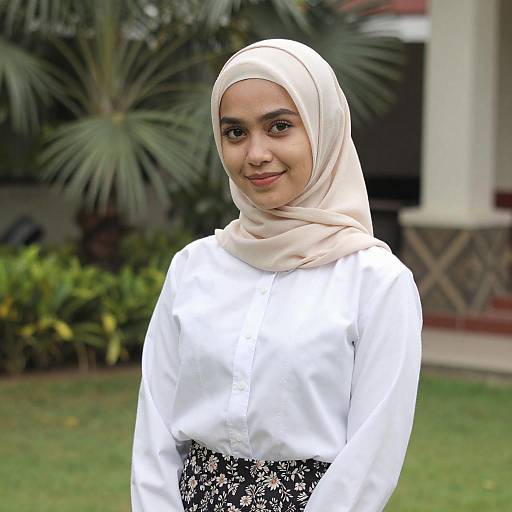 Photograph of a young Southeast Asian woman with light brown skin, wearing a beige hijab and white long-sleeve blouse with black floral skirt,