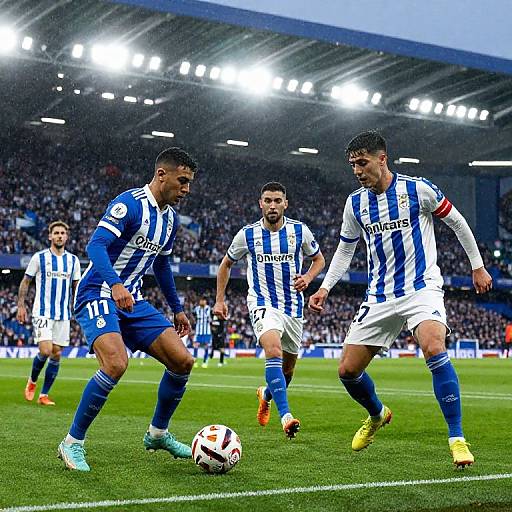 Photograph of three male soccer players in blue and white striped jerseys, with one player in blue and two in white, intensely focusing on a soccer ball