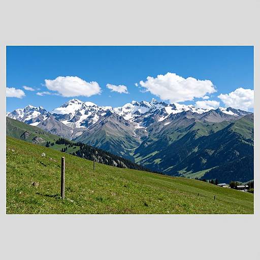 Photograph of a vibrant mountain landscape with snow-capped peaks, bright blue sky, scattered clouds, and a grassy hill with a simple wire fence