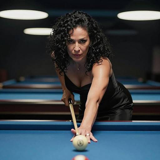 Photograph of a focused, curly-haired woman in a black dress, leaning over a blue pool table, aiming a cue stick at a ball.