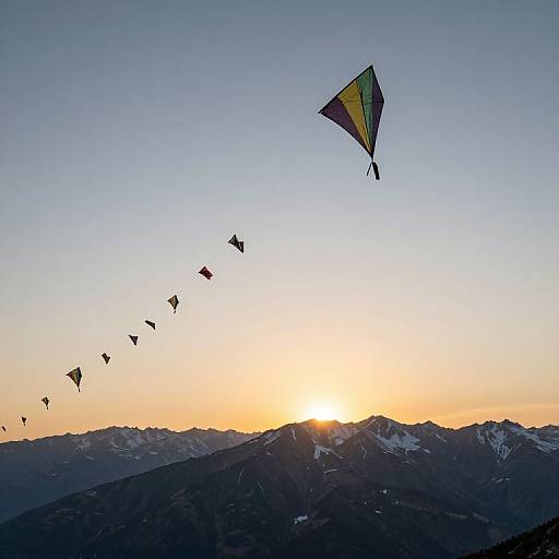 Photograph of a sunset over snow-capped mountains, with a line of colorful kites flying in the clear blue sky.