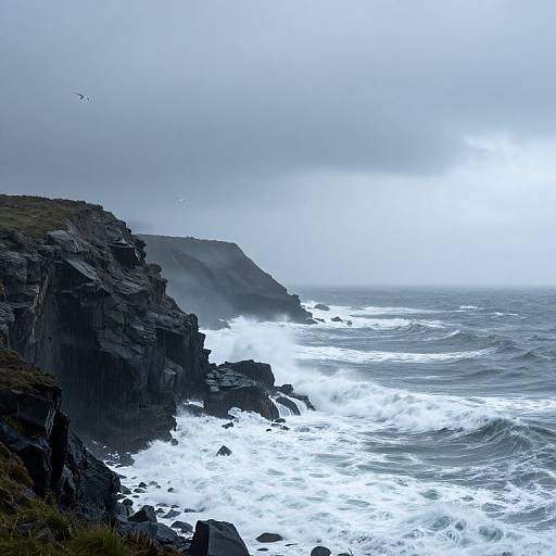 Photograph of a stormy coastal cliff with dark rocky terrain, foamy white waves crashing against the shore, and a misty, overcast sky