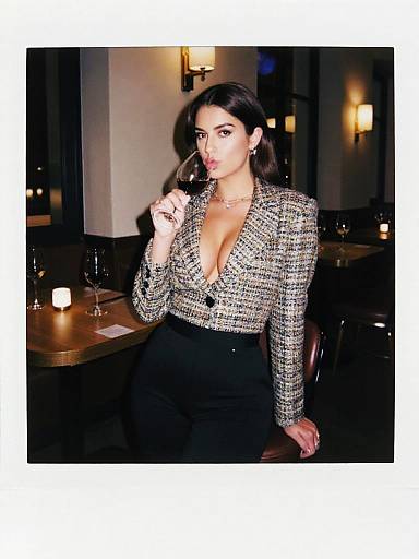 Photograph of a confident woman with long dark hair, wearing a deep V-neck, houndstooth blazer, and black pants, standing in