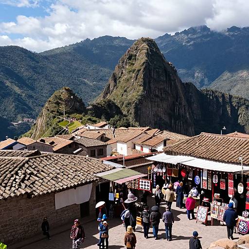 Colorful photograph of a bustling Andean market with tiled-roof buildings, people in diverse clothing, and steep, green mountainous background under a partly