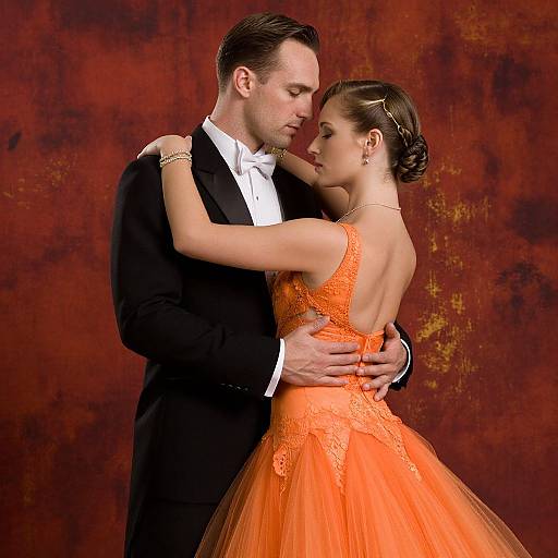 Photograph of a romantic ballroom dance couple: man in black tuxedo, woman in vibrant orange lace and tulle dress, intimate embrace,