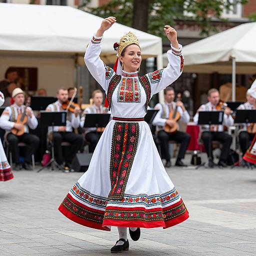 Photograph of a smiling woman in traditional Eastern European folk dress, with intricate embroidery, gold crown, white apron, and red sash, dancing