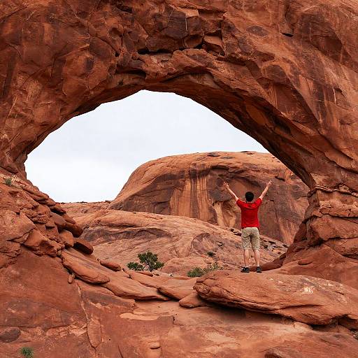 Person Standing with Raised Arms Near Red Rock Arch
