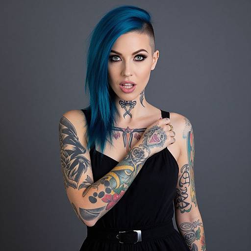 Photograph of a tattooed woman with bright blue, asymmetrical hair, black tank top, and dark background, showcasing colorful arm tattoos.