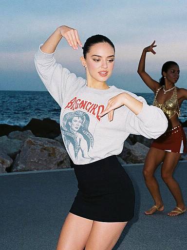 Photograph of two women dancing at a beach; foreground woman in white 
