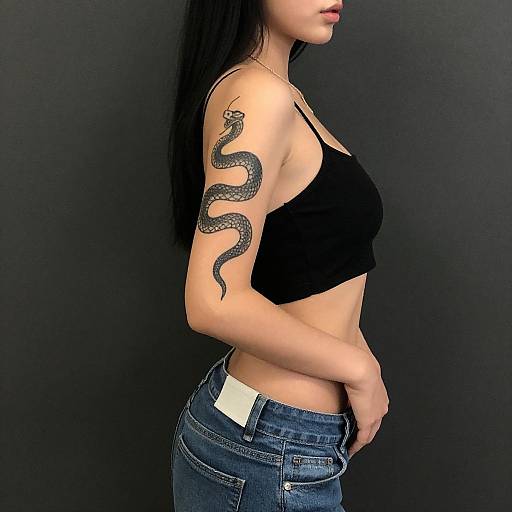 Photograph of a woman with long black hair, black crop top, and blue jeans, showing a detailed black snake tattoo on her right arm, against