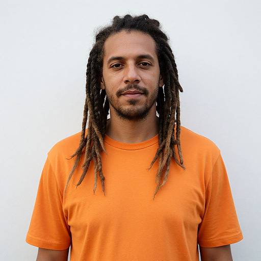 Photograph of a man with medium brown skin, long dreadlocks, and a trimmed beard, wearing an orange T-shirt, against a plain white background