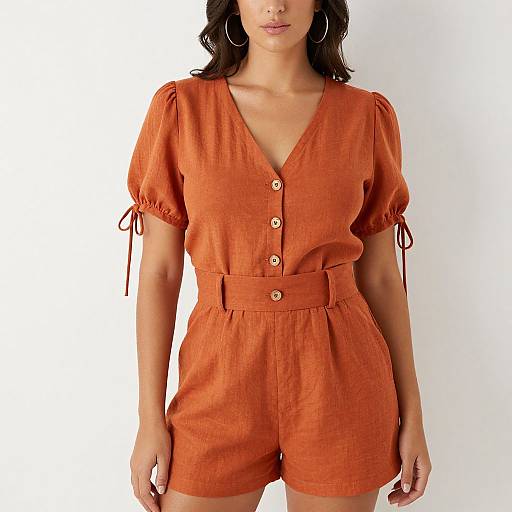Photograph of a woman with medium skin tone and dark hair, wearing an orange, short-sleeved, button-down romper with tied sleeves and