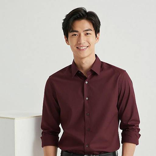 Photograph of a smiling Asian man with short black hair, wearing a dark maroon button-up shirt, standing against a plain white background.