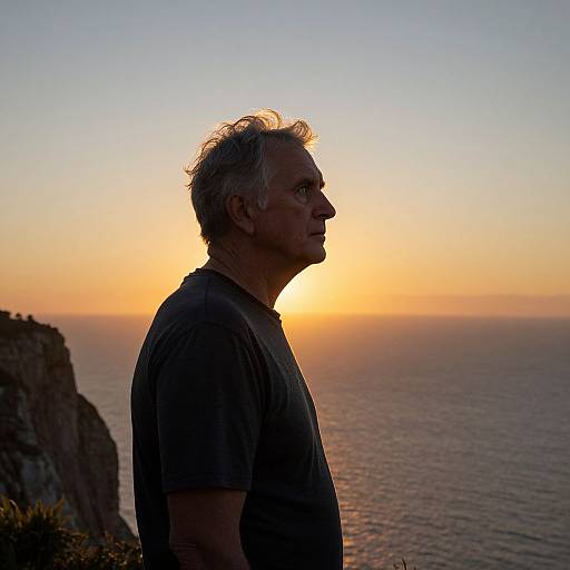 Photograph of a middle-aged man with gray hair, silhouette against a bright sunset over a calm ocean, wearing a dark t-shirt.