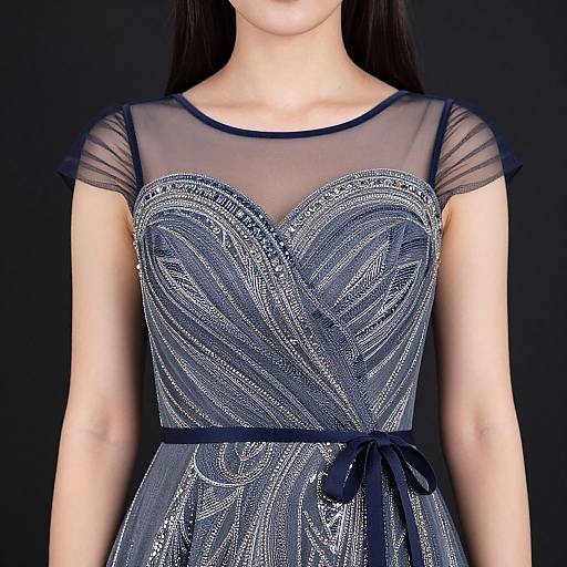 Photograph of a woman in a blue, sheer-shouldered, heart-shaped sequin dress with intricate patterns, black ribbon waist tie, against a