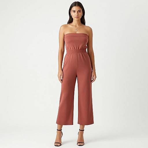 Photograph of a young woman with long black hair, wearing a strapless, red, high-waisted jumpsuit, black sandals, and a