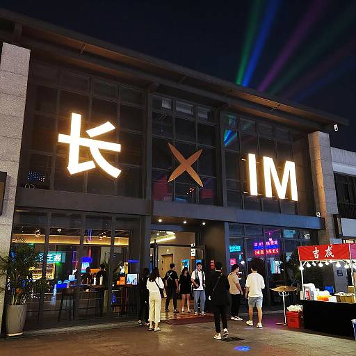 Nighttime photograph of a modern IMAX theater entrance with illuminated Chinese characters, people in casual attire, and neon signs.